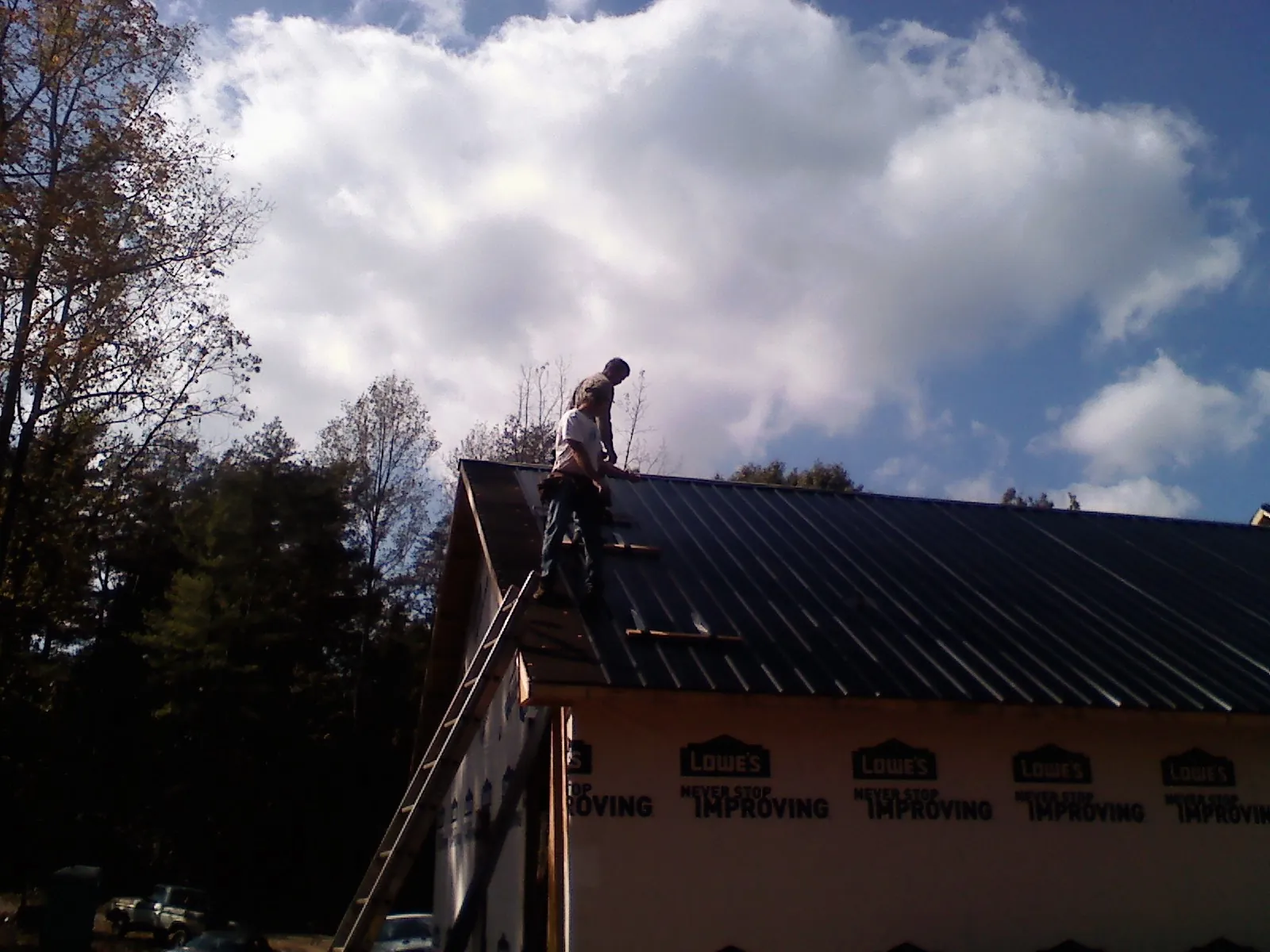 Roofer fastening dark metal panels high against a cloudy sky, from a Roof Inspection job in Ellington