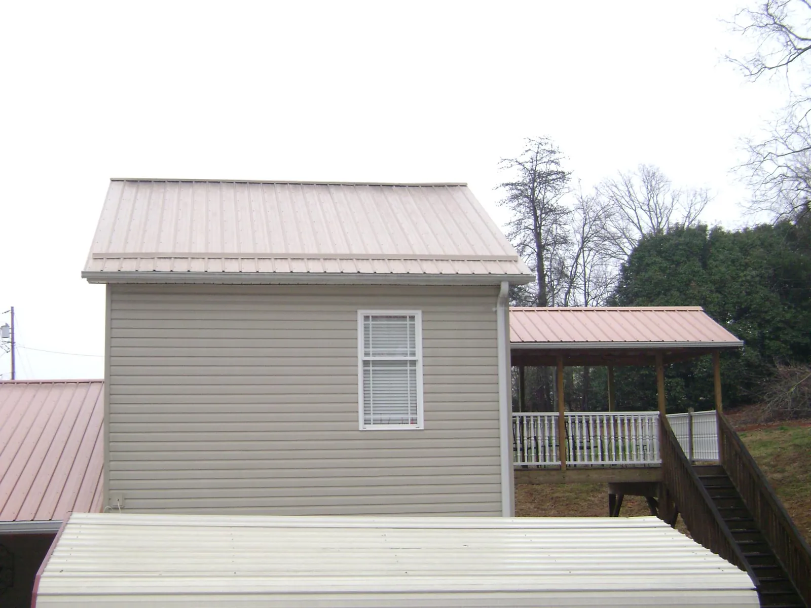 Tan metal roofs on a two story addition and attached porch, from a Roof Replacement job in Ellington